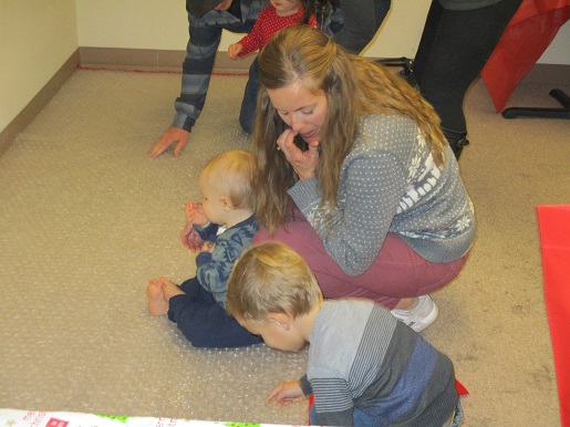 A mother and her children are checking out the poping sound on the floor made from packing material